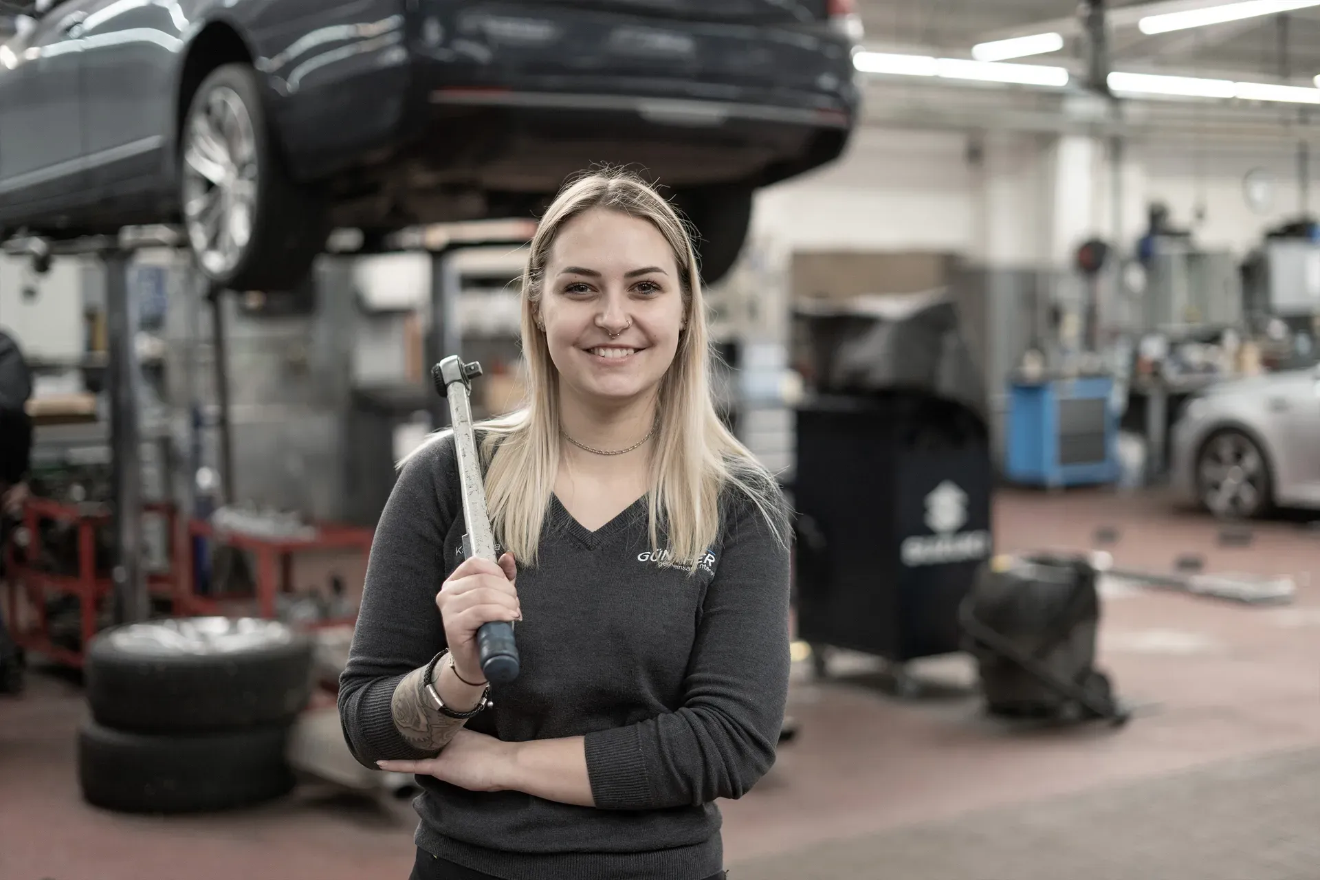 Kfz-Technikerin von Auto Günther mit Drehmomentschlüssel in der Werkstatt, dahinter ein Fahrzeug auf der Hebebühne