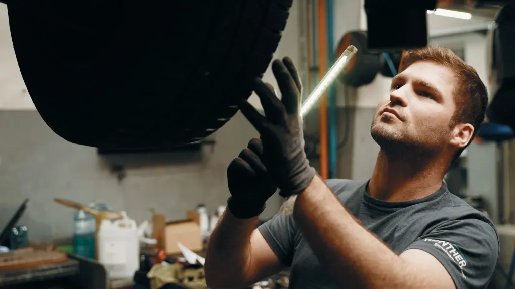 Techniker von Auto Günther prüft mit Arbeitsleuchte ein Rad am angehobenen Fahrzeug
