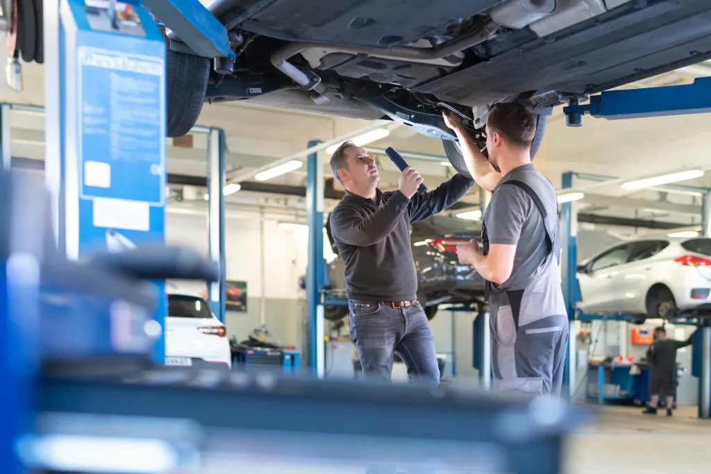 Werkstatt-Team prüft ein Fahrzeug auf der Hebebühne mit Arbeitsleuchte